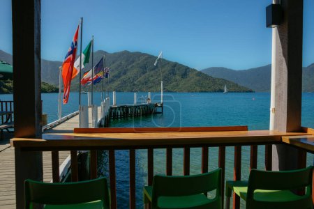Téléchargez les photos : Quai avec des drapeaux projetant dans la baie pittoresque entourée de collines bush vêtus de Marlborough Sounds, Nouvelle-Zélande. - en image libre de droit