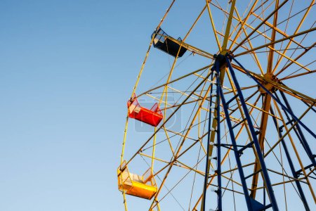 Téléchargez les photos : Old-fashioned ferris wheel with yellow and red seat against blue sky. - en image libre de droit