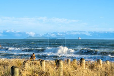 Foto de Mount Maunganui New Zealand - January 9 2022: Woman on beach as cruise ship arriving at Mount Maunganui on horizon beyond breaking waves - Imagen libre de derechos