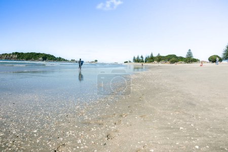 Photo for Background wide angle summer beach image with man carrying surfboard along waters edge at Mount Maunganui - Royalty Free Image