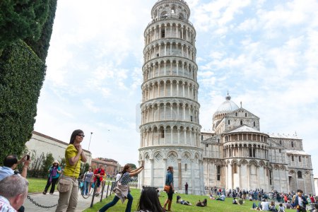 Photo for Pisa Italy - April 24 2011; Editorial-Tourists in square around famous Leaning Tower of Pisa tourists holding top. - Royalty Free Image