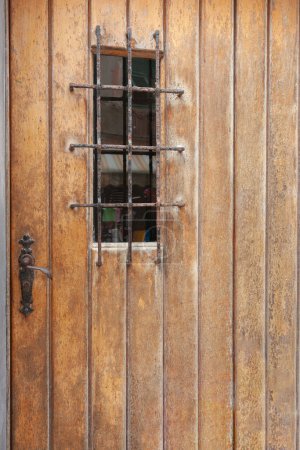 Foto de Puerta de madera rústica con mango oxidado y rejilla de seguridad en composición vertical. - Imagen libre de derechos