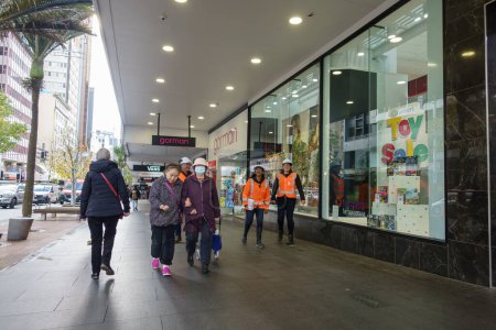 Foto de Auckland Nueva Zelanda - 2 de julio de 2023; Mujeres brazo en brazo y trabajadores en chalecos de color naranja de alta visibilidad en la calle urbana. - Imagen libre de derechos