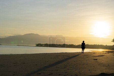 Téléchargez les photos : Denarau Fidji - 4 septembre 2023 ; figure lointaine méconnaissable d'une personne seule en silhouette s'éloignant sur une plage tropicale au lever du soleil. - en image libre de droit