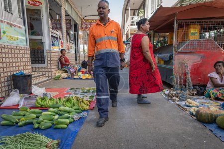 Téléchargez les photos : Sigatoka Fidji - 8 septembre 2023 ; Homme en gilet de travailleur orange marche sur le bain entre les produits disposés sur des feuilles de plastique à vendre. - en image libre de droit