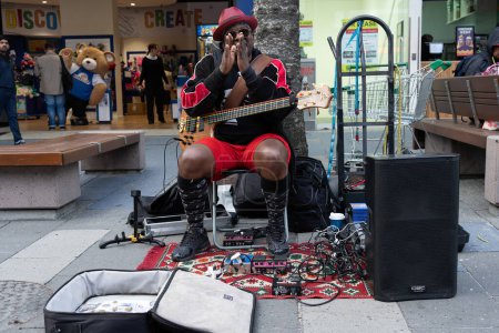 Photo for Surfers Paradise Australia; September 23 2023; Colorfully attired black man on street  busking guitarist on Cavill Mall  hoping for money with five string base clapping his hands. - Royalty Free Image