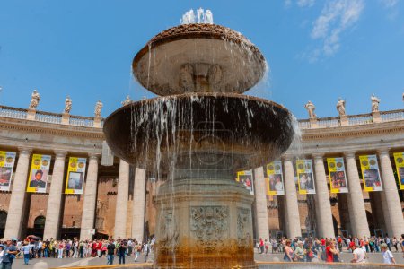 Photo for Rome Italy - May 21 2011; Editorial- St Peter's courtyard and large fountain with crowd of tourists surrounded by famous colonnade with banners of past popes and with statues of saints around top. - Royalty Free Image