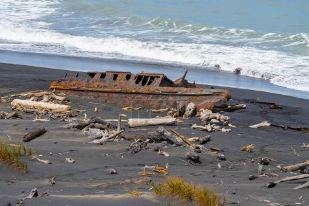 Old wrecked hulk of washed-up boat rusty and surrounded by driftwood in Patea Coastal South Taranaki , New Zealand.