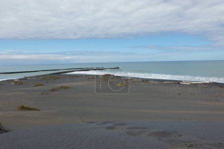 Schritte, die entlang schwarzer Sanddünen zum Wasserrand von Patea, Neuseeland, führen.