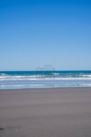 Opunake playa de surf con la costa oeste de arena negra, cielo azul y agua.