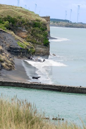 Karge Klippen südlich von Patea mit Windrädern in der Ferne, Neuseeland.