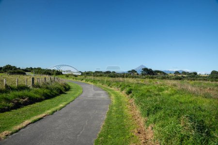 Land and track leading to bridge in foreground and mountain behind white steel Te Rewa Rewa Bridge landmark on Coastal Walkway in New Plymouth Taranaki.