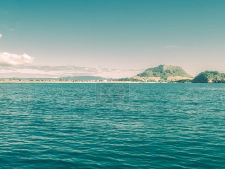 Fade effect summer vibes tones of Mount Maunganui landmark beyond blue sea and clear blue sky.