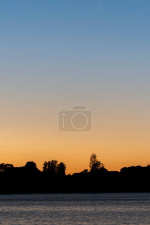 Silhouette terre et arbres à l'horizon sous le ciel coloré du lever du soleil à travers le port de tauranga.