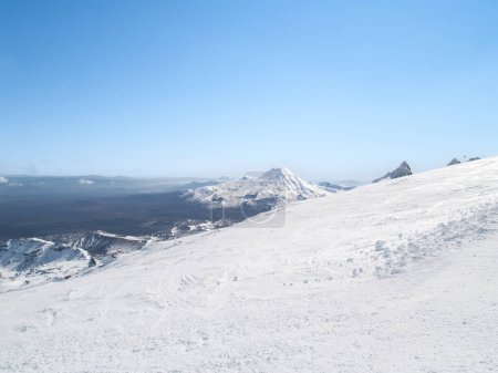 Expansive view from snow-clad Mount Ruapehu across landscape and two mountains in Tongariro National Park.