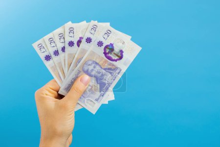Téléchargez les photos : Image woman's hands which holds British pounds in her hands isolated over blue studio background - en image libre de droit