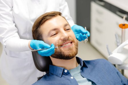 Photo for Portrait of happy man sitting at dentist chair in modern clinic and smiling. Patient enjoying dental treatment with professional stomatolog. - Royalty Free Image