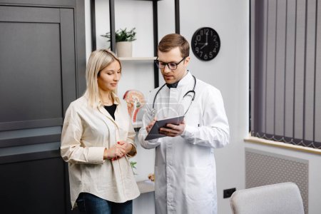 Photo for Happy man doctor showing tablet woman patient in clinic office interior. Health care, visit to family therapist, treatment of illness and medical help. - Royalty Free Image