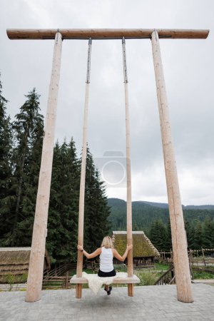 Photo for A woman sits on a huge swing and contemplates a beautiful view of the mountains. Famous huge swing in Carpatian mountains - Royalty Free Image