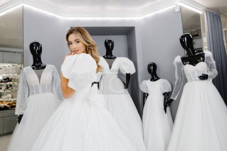 Téléchargez les photos : Jolie jeune femme choisit une robe de mariée dans la boutique. La future mariée porte une robe de mariée pour s'adapter. - en image libre de droit