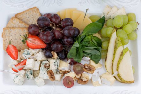 A white plate is laid out with a variety of grapes, cheese, and crackers, creating a simple and elegant snack arrangement.