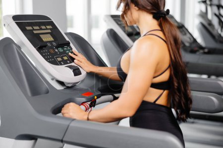 Attractive young sports woman is working out in gym, she doing cardio training on treadmill. Running on treadmill