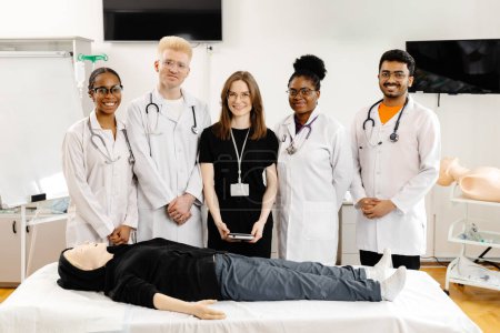 Un groupe de professionnels de la santé en blouse blanche debout autour d'un mannequin allongé sur un lit d'hôpital, semblant discuter de son état ou de son traitement.
