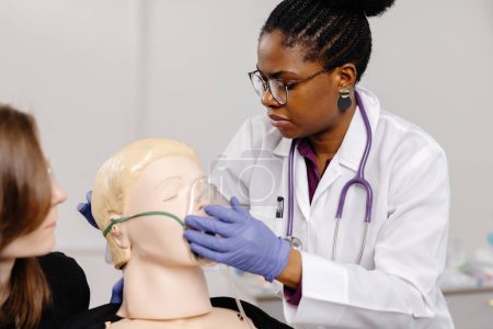 A female doctor is carefully examining the head of a mannequin, likely practicing medical procedures or demonstrating techniques in a clinical setting.
