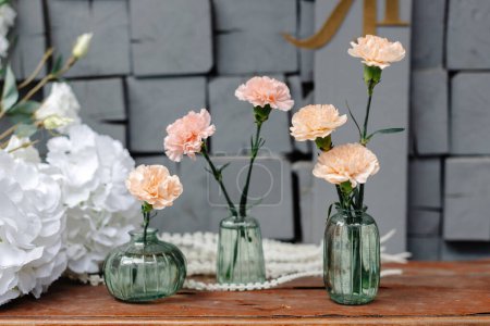 Drei Vasen, gefüllt mit verschiedenen Blumen, stehen säuberlich auf einem Tisch. Die leuchtenden Farben der Blüten stehen im Kontrast zur neutralen Tischplatte.