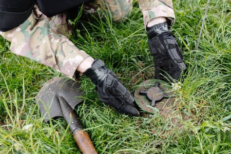 Ein Mann in Militäruniform und schusssicherer Weste arbeitet im Wald, um das Gebiet zu entminen. Ein Mann entschärft eine Antipersonenmine.