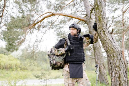 Young soldier in uniforms and tactical vest works in the forest and prepares for action at a temporary forest base. A man does in the work of demining the territory.