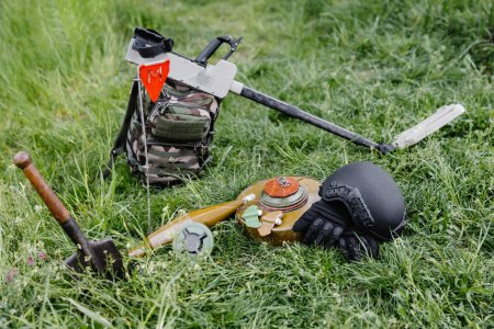 Explosive devices and a metal detector lie on the background of a forest massif. Equipment for demining the territory.