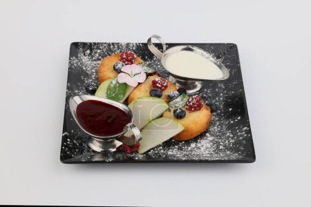 Syrnyky aus Quark mit Beerenmarmelade, saurer Sahne und Beere auf dunklem Teller auf weißem Hintergrund.