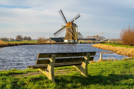 Molino de viento holandés tradicional en Baambrugge con el río Angstel y banco vacío, espacio para copiar