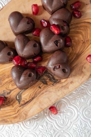 Herzförmige Schokolade und Granatapfelbonbons auf einem Olivenholzbrett.  