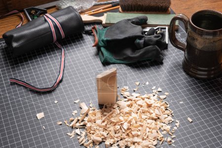 Photo for Carving tools on a cutting mat with basswood, shavings, gloves, knives roll, and coffee mug. - Royalty Free Image