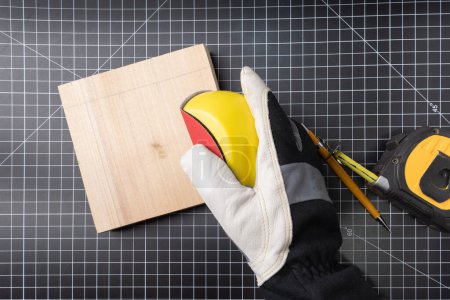 Téléchargez les photos : Main gantée utilisant un bloc de ponçage pour poncer une pièce de projet en bois. - en image libre de droit
