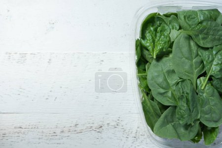 Photo for Clear, plastic container holding fresh spinach.  White, wooden background. - Royalty Free Image