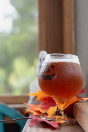 Pumpkin beer in jack-o-lantern glass sitting on ledge of an outdoor seating area of a restaurant bar.