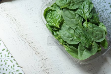 Photo for Clear, plastic container holding fresh spinach. small, green leaf and white tray. - Royalty Free Image