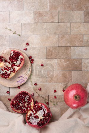 Photo for Fresh, ripe pomegranate and a cup of hot tea on earth-tone colored tile background.  Selective focus. - Royalty Free Image