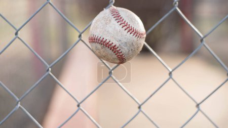 Foto de Una pelota de béisbol bien gastada en una cerca encadenada con un fondo de enfoque suave. - Imagen libre de derechos