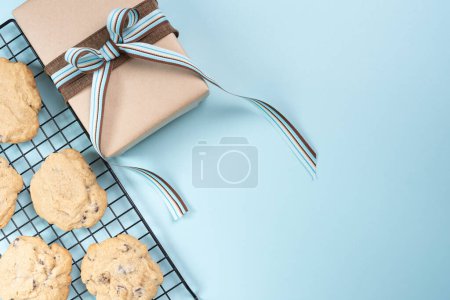 Gift wrapped and lying beside of fresh baked chocolate chip cookies. Light blue background.