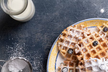 Photo for Waffles, blueberries, and powdered sugar with milk on a textured blue table. - Royalty Free Image