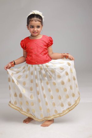 Téléchargez les photos : Une jolie petite fille enfant portant une jupe longue Kerala couleur or et chemisier rouge, image isolée avec fond blanc. - en image libre de droit