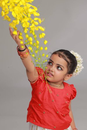 Foto de Una linda niña pequeña con Kerala vestido de color dorado falda larga y blusa roja con flor de ducha de oro, aislado - Imagen libre de derechos