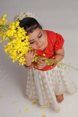 Téléchargez les photos : Une jolie petite fille enfant portant une jupe longue Kerala couleur or et une blouse rouge avec une fleur de douche dorée, isolée - en image libre de droit