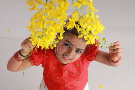 Foto de Una linda niña pequeña con Kerala vestido de color dorado falda larga y blusa roja con flor de ducha de oro, aislado - Imagen libre de derechos
