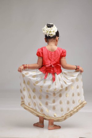 Téléchargez les photos : Une jolie petite fille enfant portant une jupe longue Kerala couleur or et chemisier rouge, image isolée avec fond blanc. - en image libre de droit