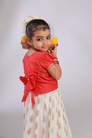 Téléchargez les photos : Une jolie petite fille enfant portant une jupe longue Kerala couleur or et chemisier rouge, thème du festival onam, fond blanc isolé. - en image libre de droit